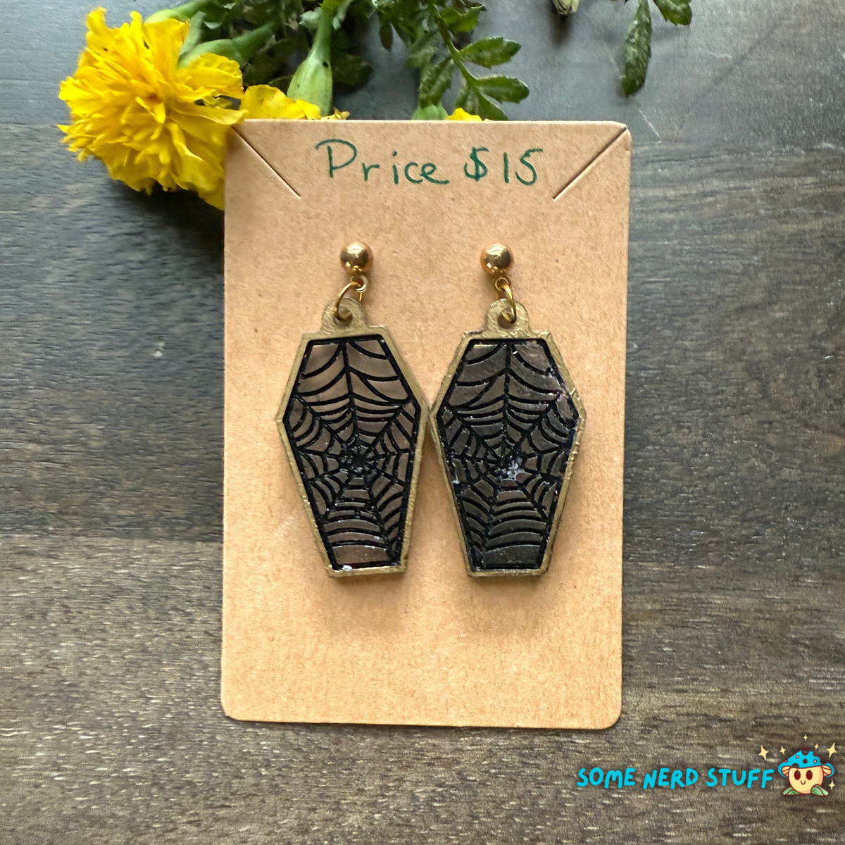Spider web earrings on a display card with a price tag of $15 and yellow flower in the background sold on SomeNerdStuff.com