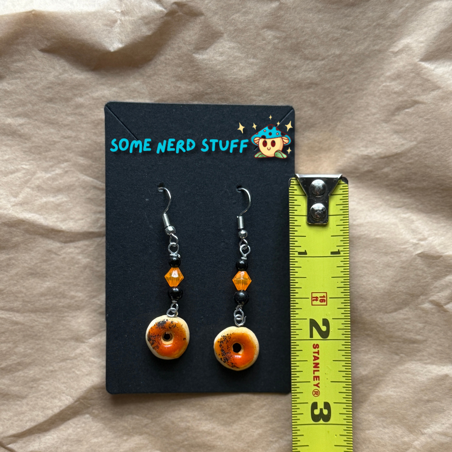Blood Orange Polymer Clay glazed earring topped with beads shown with measuring tape for size