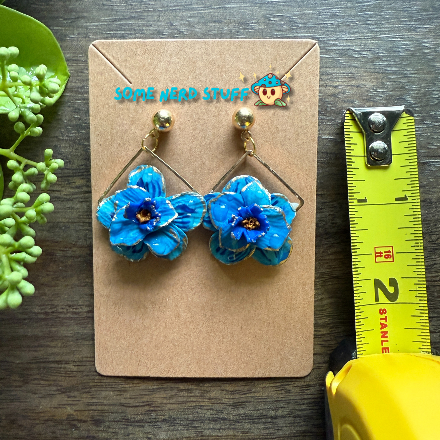 Manga Frieren: Beyond Journey's End Inspired Blue Moon Flower Polymer clay with gold highlighted earrings shown with measuring tape made by SomeNerdStuff