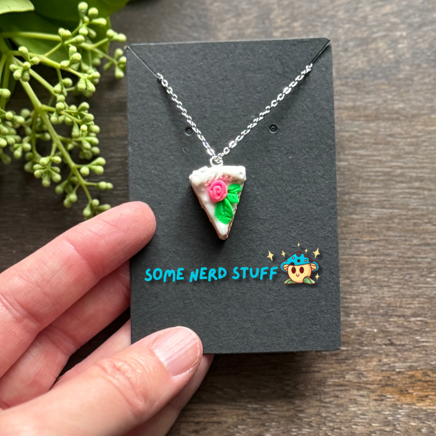 Pretty in Pink Polymer Clay necklace top view with pink rose and green petals shown in hand for size
