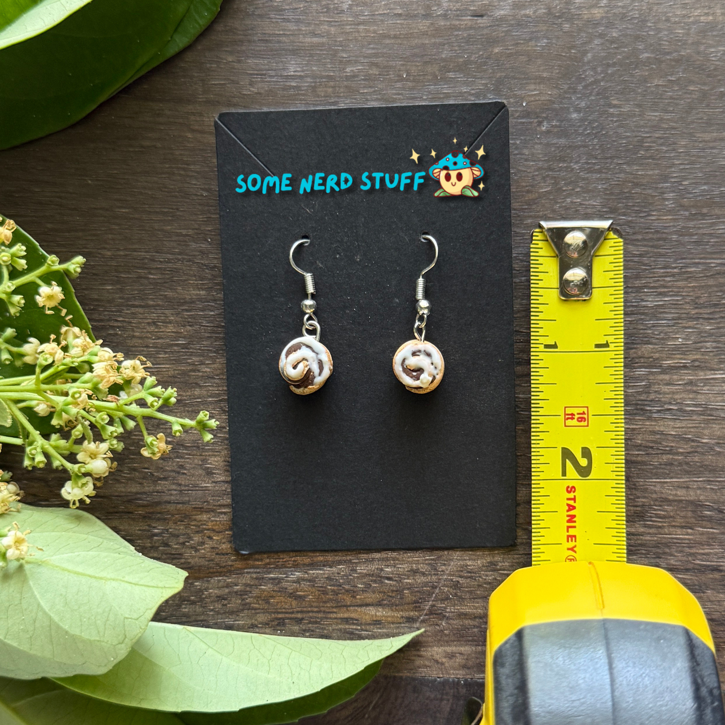 Cinnamon roll earrings made from polymer clay and resin shown in hand for size by SomeNerdStuff