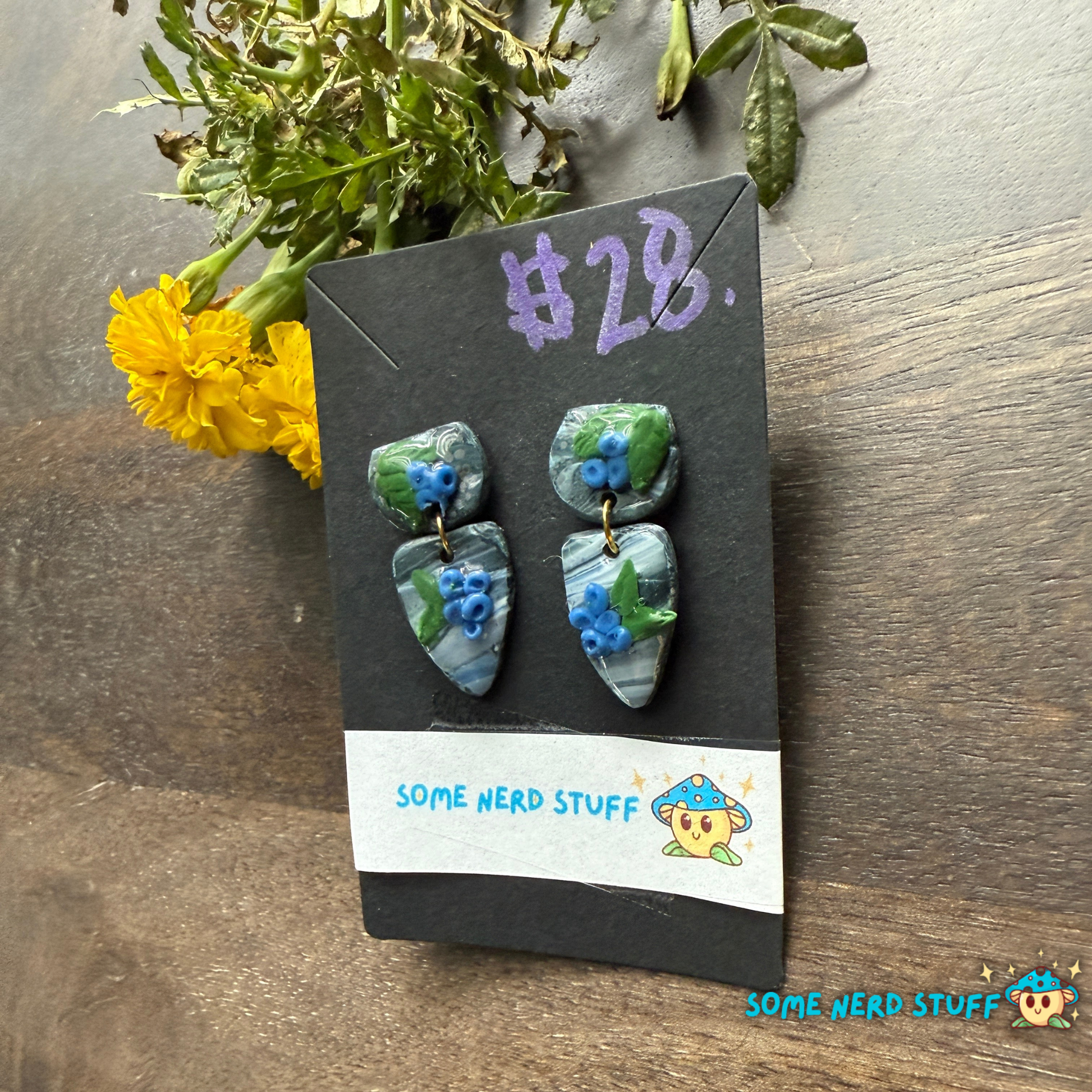 Pair of blueberry and faux stone handmade polymer clay earrings on a 'Some Nerd Stuff' branded card with flowers in the background.