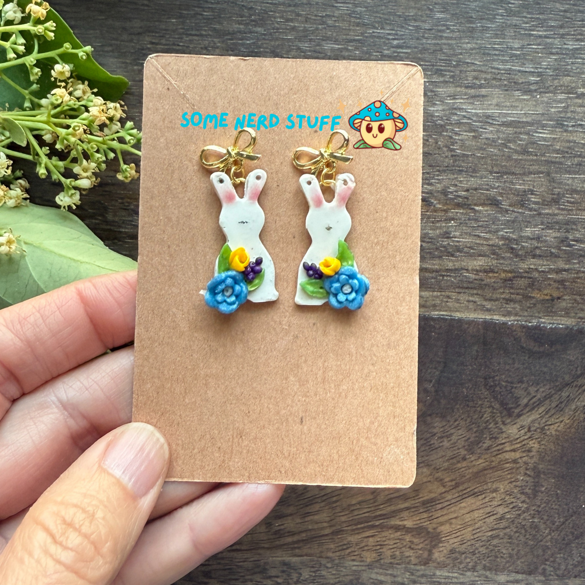 Bunny Polymer clay earrings with petite blue and yellow flwoers topped with a bow post shown in hand for scale.