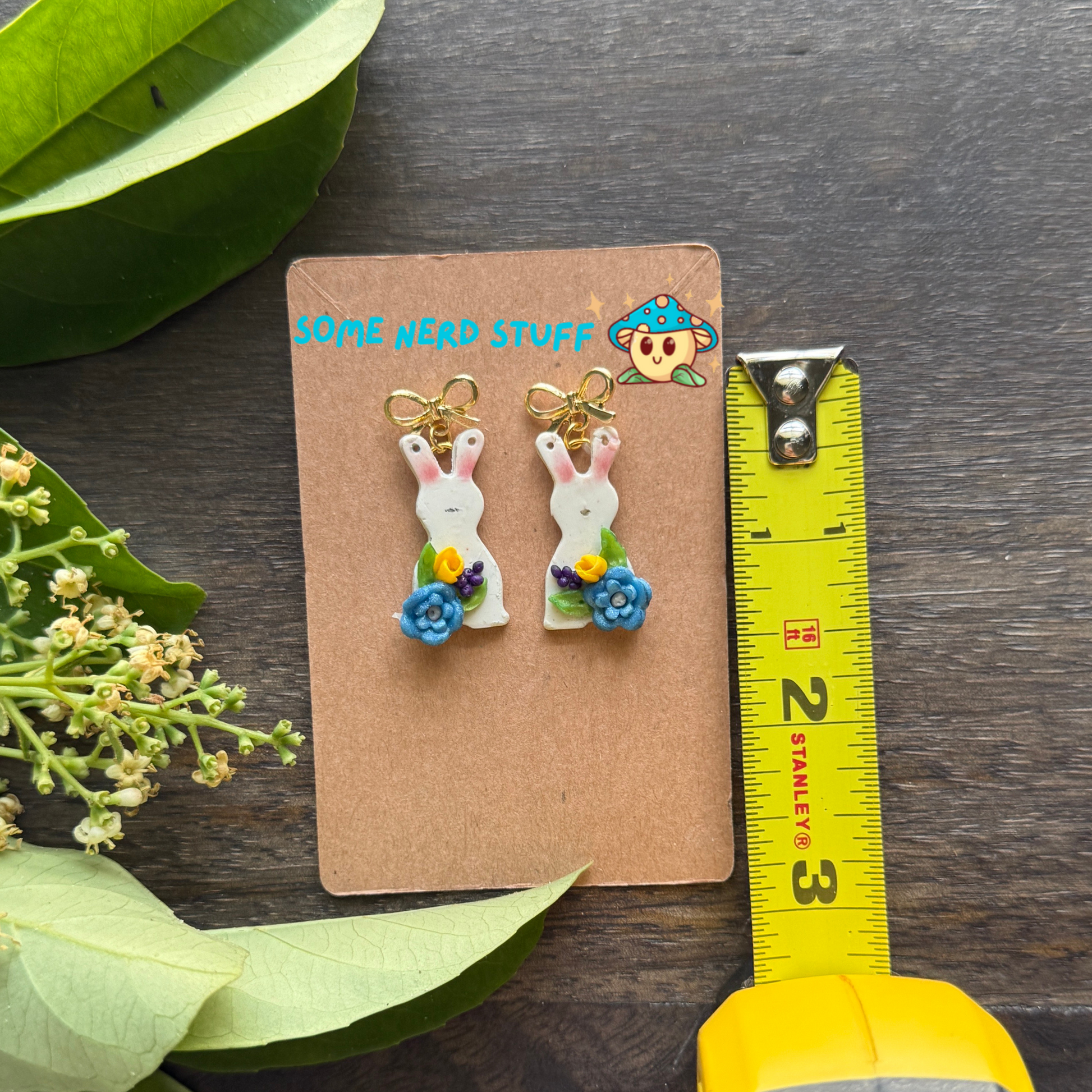 Bunny Polymer clay earrings with petite blue and yellow flwoers topped with a bow post shown with measuring tape.