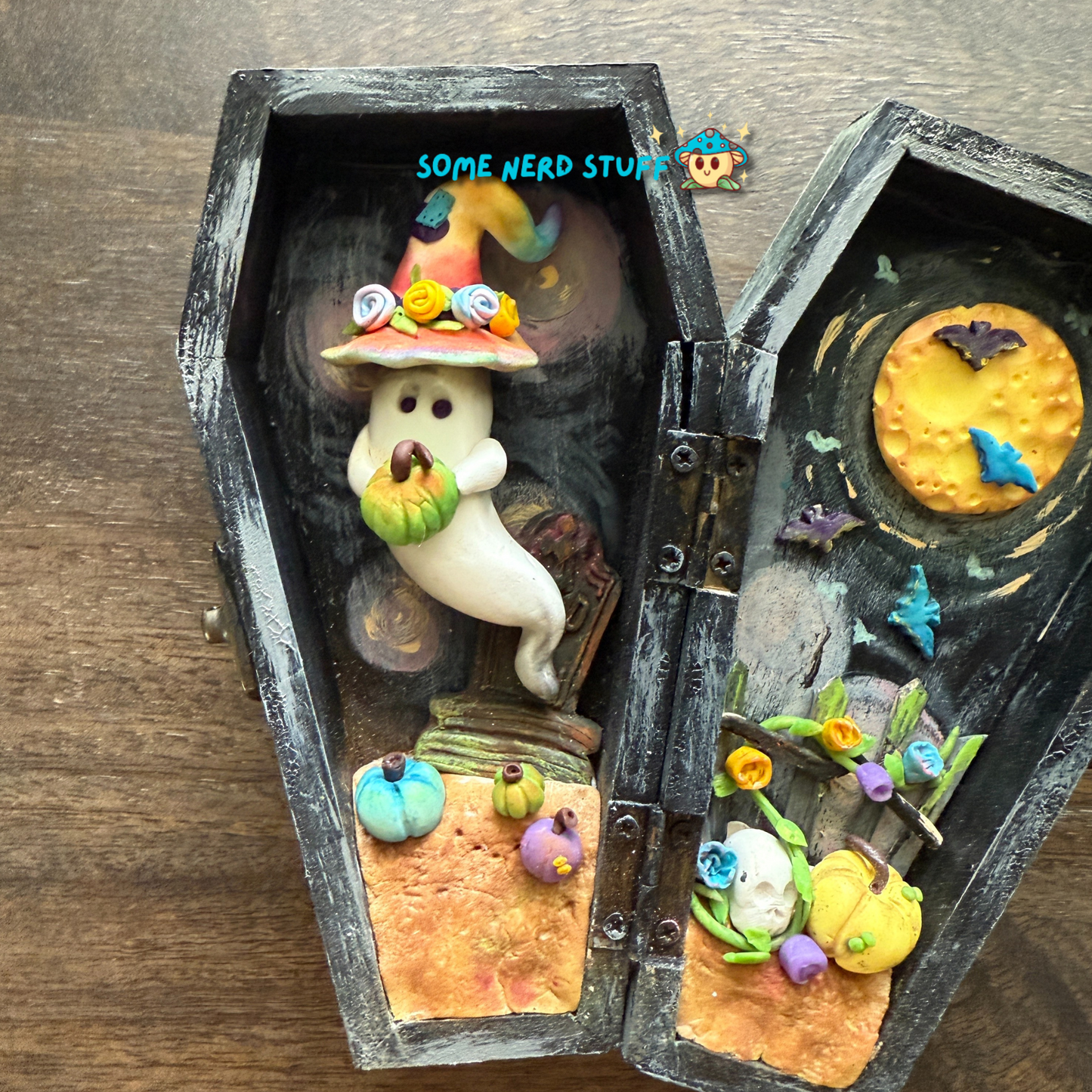 Wooden craft coffin decorated with  polymer clay ghost topped with a patchwork witch hat, mini pumpkins, tombstone, bats over the moon, and so much more.