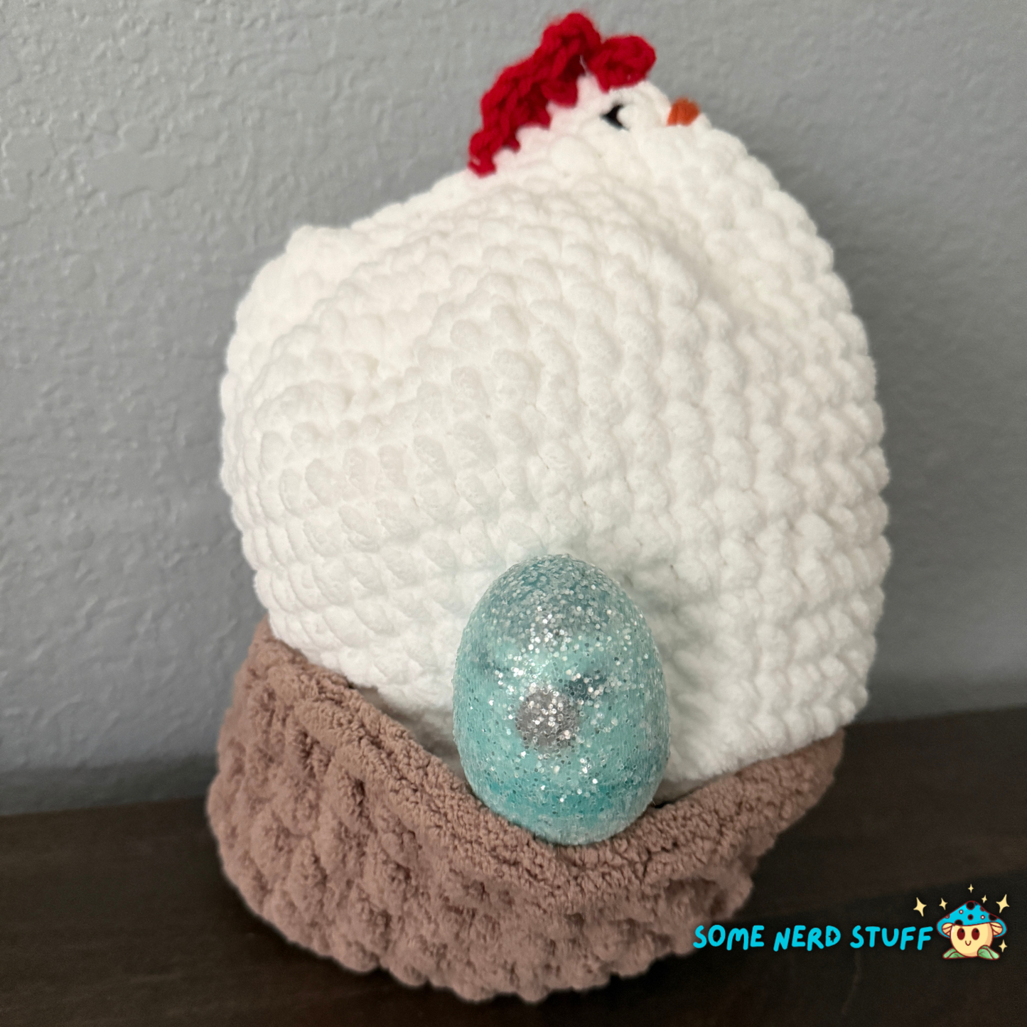 Crocheted chicken DIxie with baby cluck chick and holds a fun glitter egg all sitting on a ultra soft crocheted nest sold by SomeNerdStuff