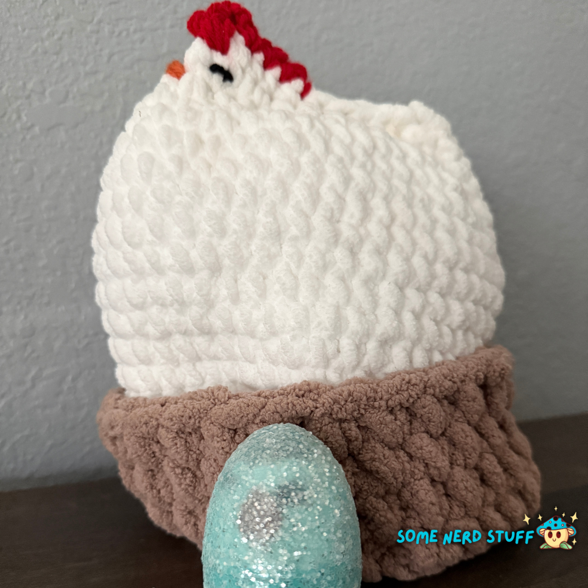 Crocheted chicken DIxie with baby cluck chick and holds a fun glitter egg all sitting on a ultra soft crocheted nest sold by SomeNerdStuff