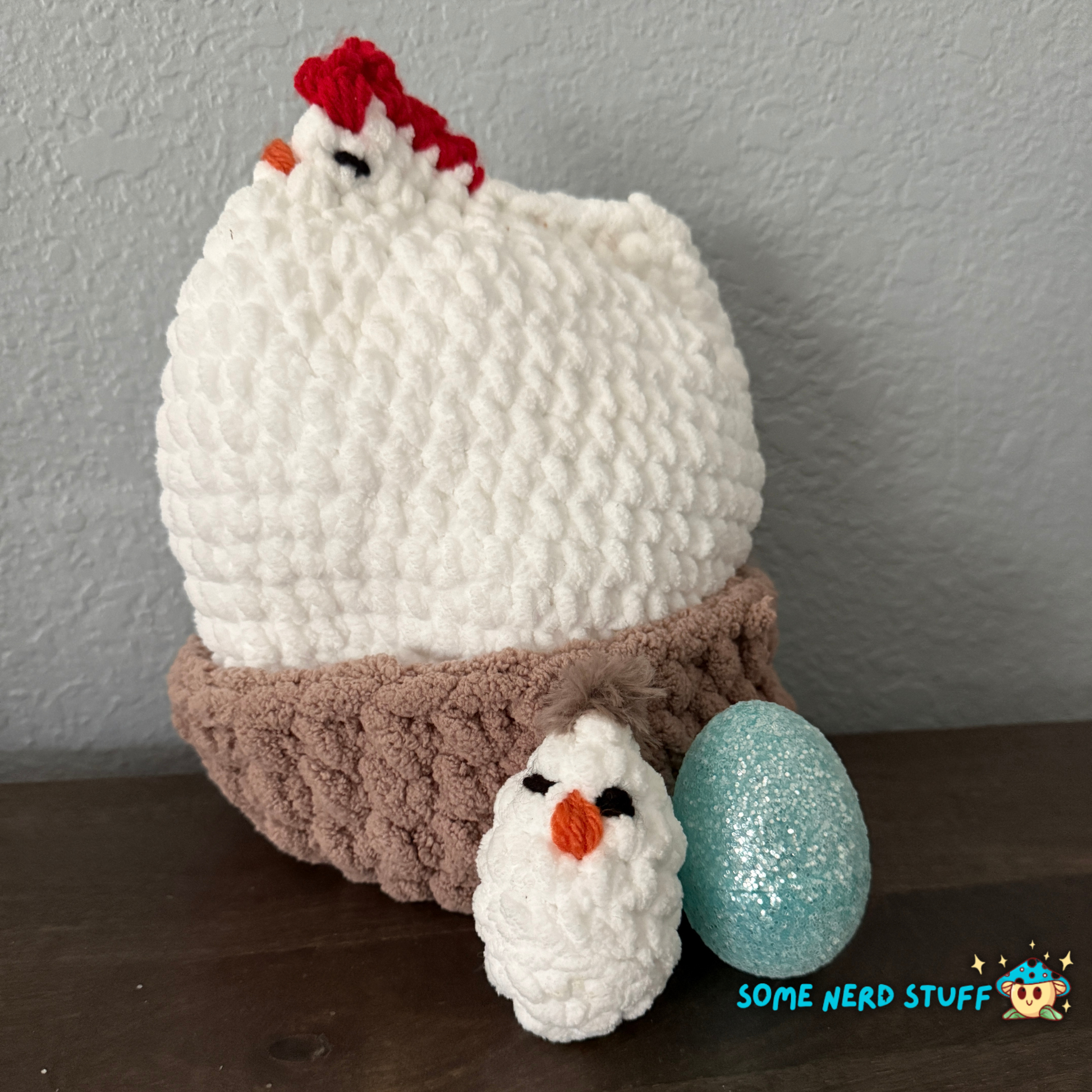 Crocheted chicken DIxie with baby cluck chick and holds a fun glitter egg all sitting on a ultra soft crocheted nest sold by SomeNerdStuff