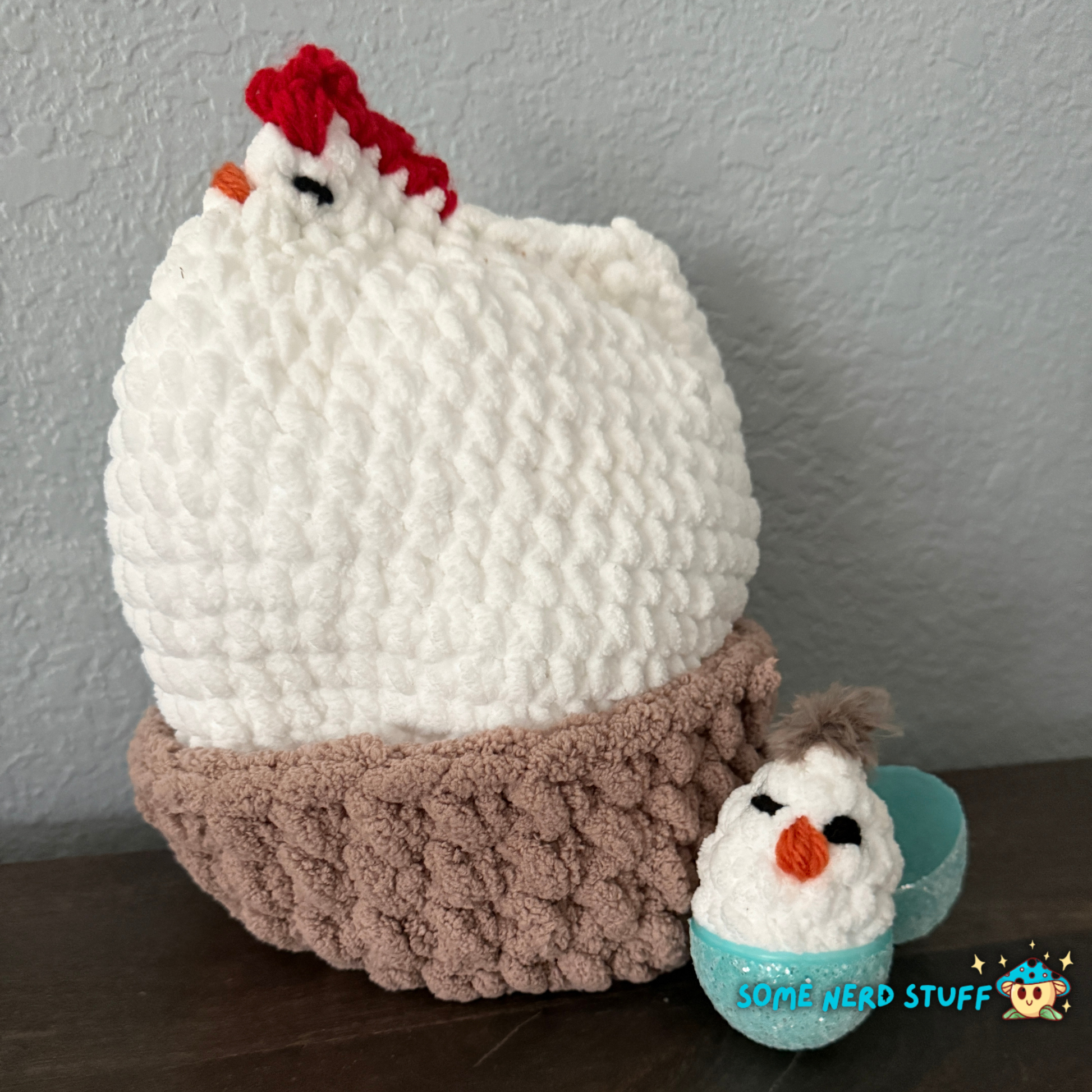 Crocheted chicken DIxie with baby cluck chick and holds a fun glitter egg all sitting on a ultra soft crocheted nest sold by SomeNerdStuff
