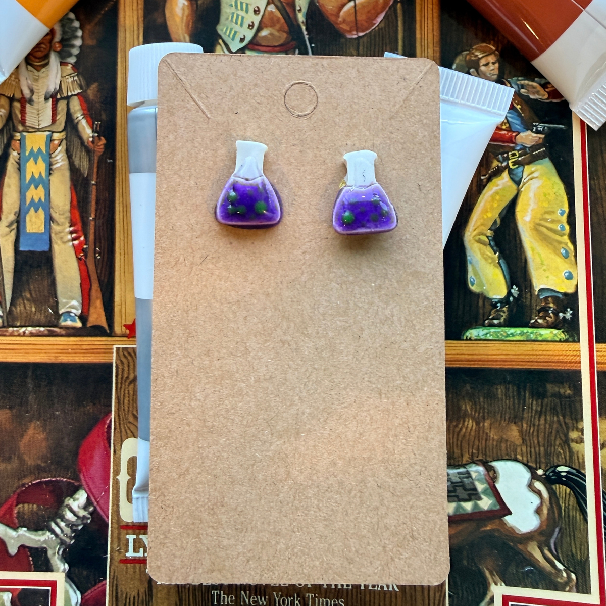 Pair of purple beaker stud earrings with white necks and green bubble details on a kraft card.