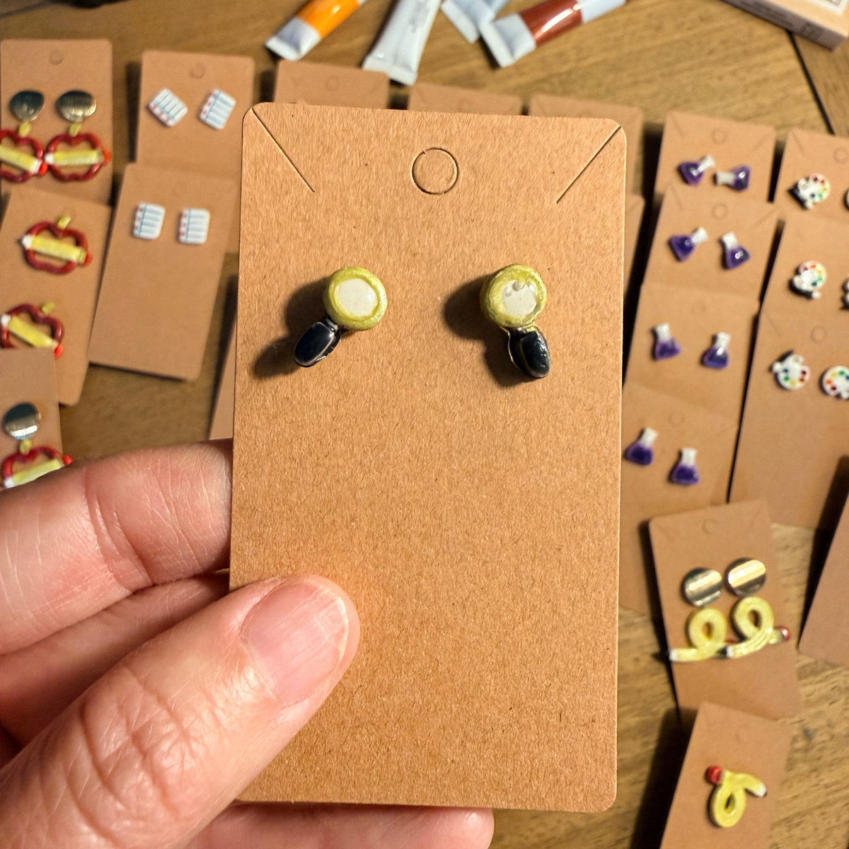 Hand holding magnifying glass stud earrings with round gold-tone rims and black handles.