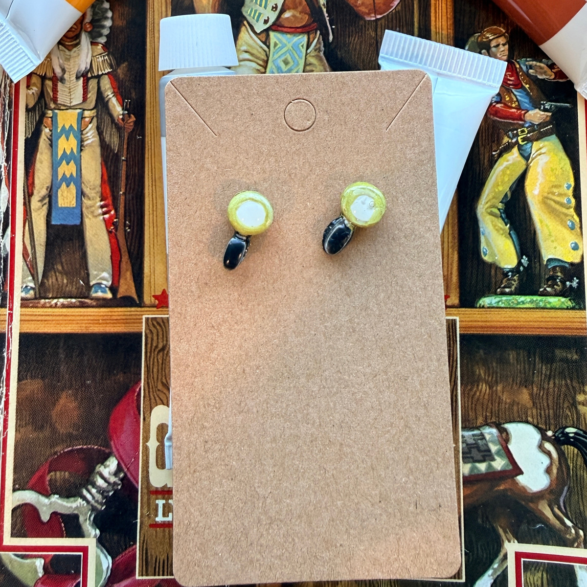 Matching magnifying glass stud earrings with pale centers and black handles on a kraft card.