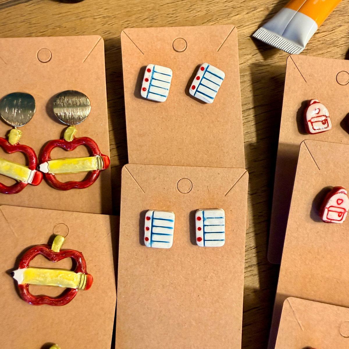 White notebook paper stud earrings with blue lines and red margin details displayed on kraft cards.