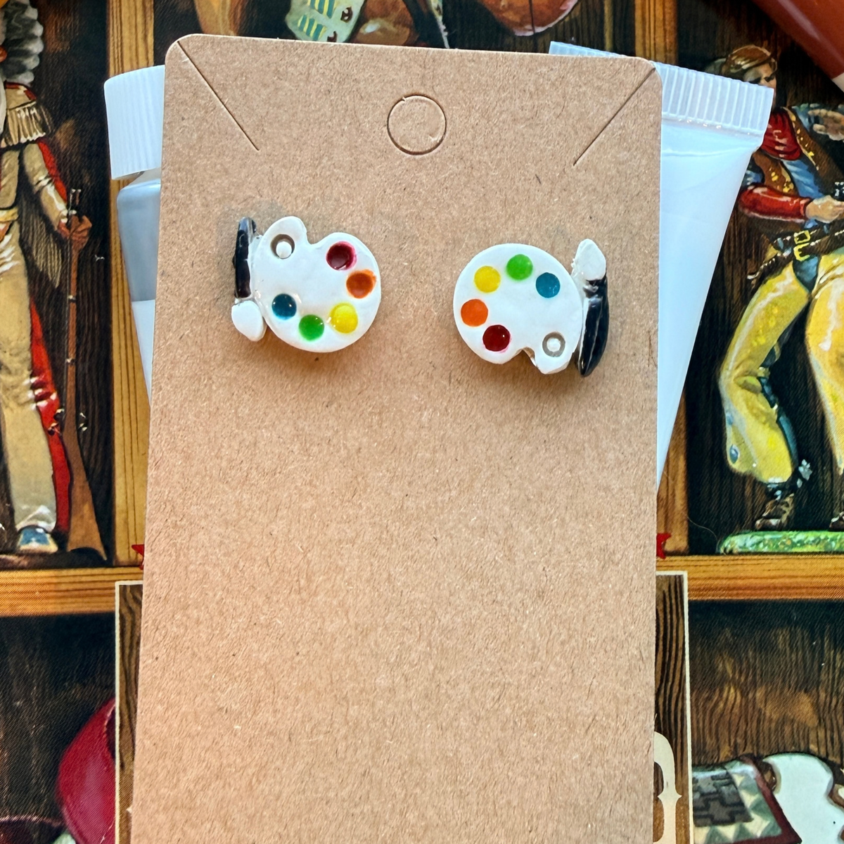 Pair of white paint palette stud earrings with colored paint dots and black brush details.