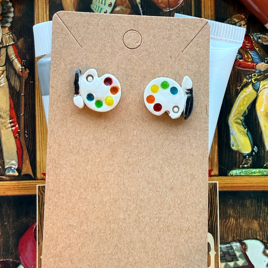 Pair of white paint palette stud earrings with colored paint dots and black brush details.