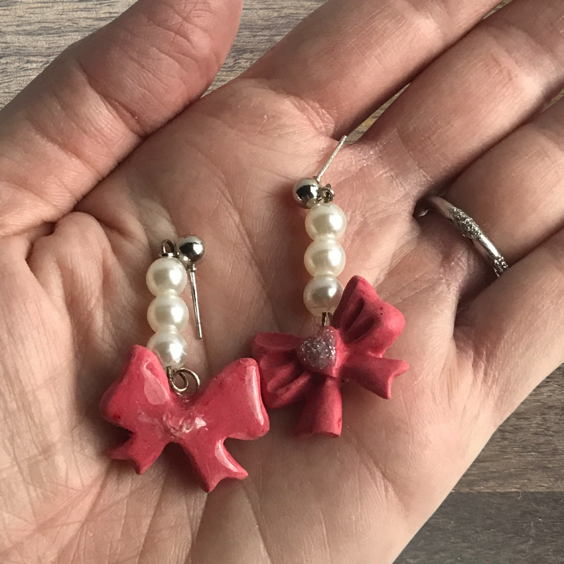 Polymer Clay pink bows with pearl danging earrings shown in hand to show size made by SomeNerdStuff