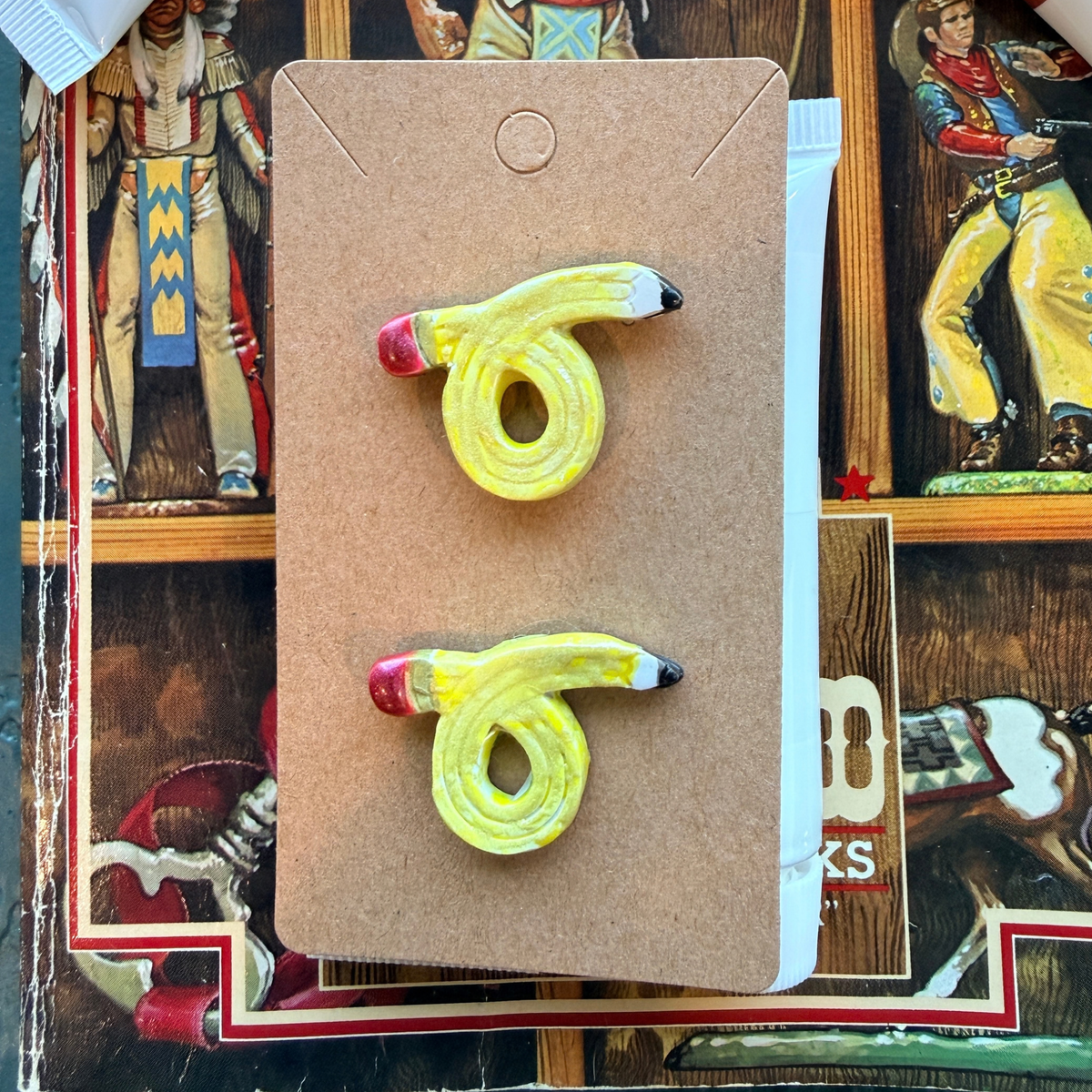 Pair of looped yellow pencil stud earrings with red eraser details and dark points.