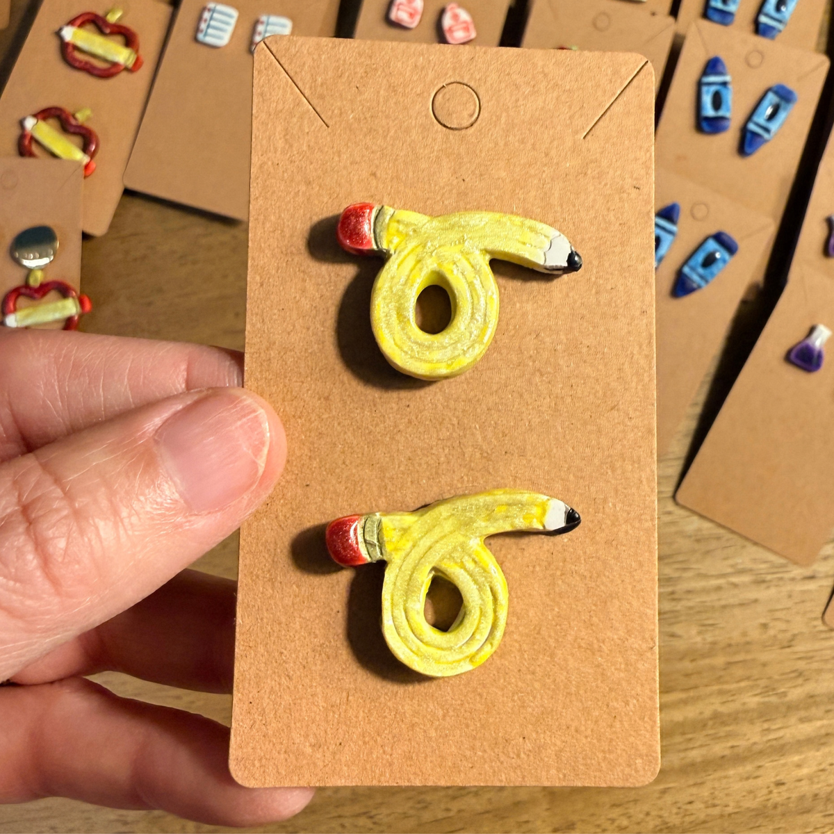 Hand holding a card with looped yellow pencil stud earrings featuring red eraser details.