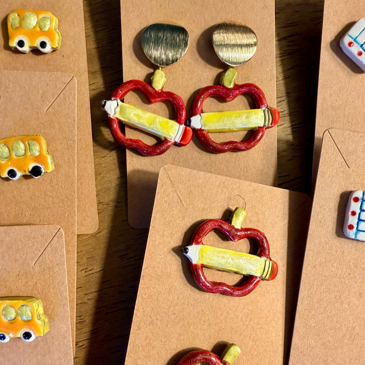 Apple and pencil dangle earrings with round gold-tone tops, displayed above matching apple studs.