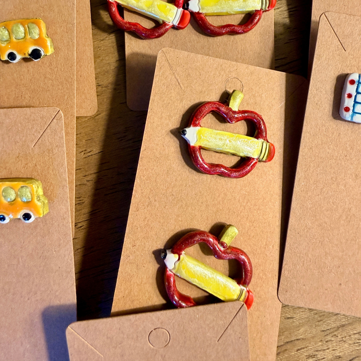 Red apple and yellow pencil stud earrings displayed beside other school-themed earrings.