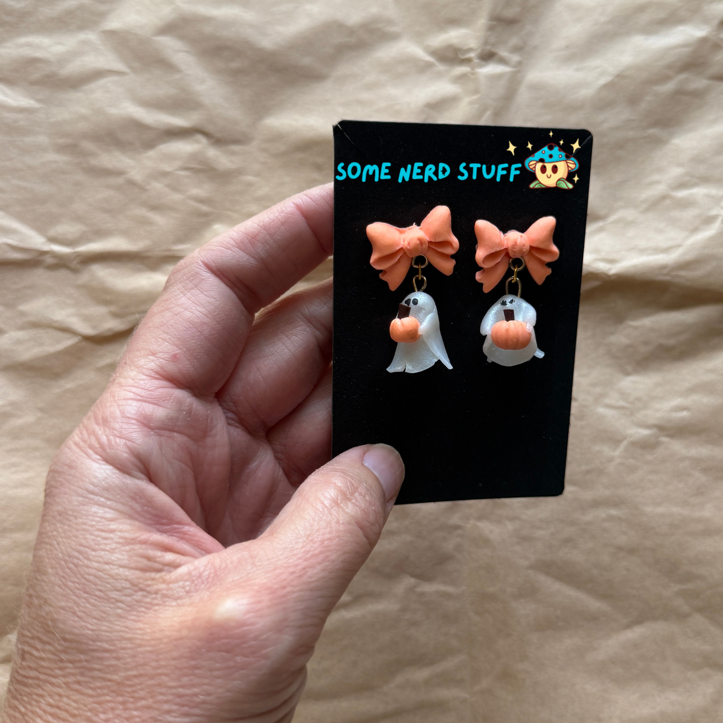 Polymer Clay Stud earrings with peach bows, phantoms holding pumpkins hand holding them to show size made by SomeNerdStuff