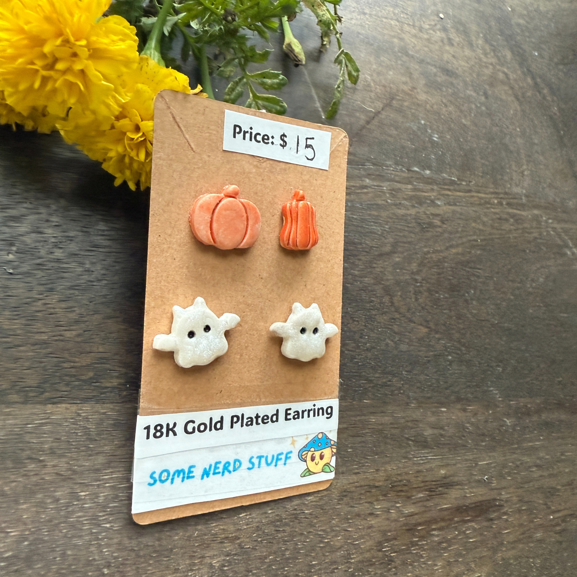 Pumpkin and ghost earrings on a 'Some Nerd Stuff' card with price tag, on a wooden surface.