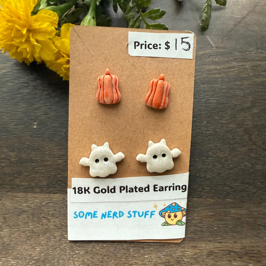 Halloween-themed earrings on a cardboard backing with a price tag, on a wooden surface featuring pumpkins and flying ghosts 18k gold plated earrings.