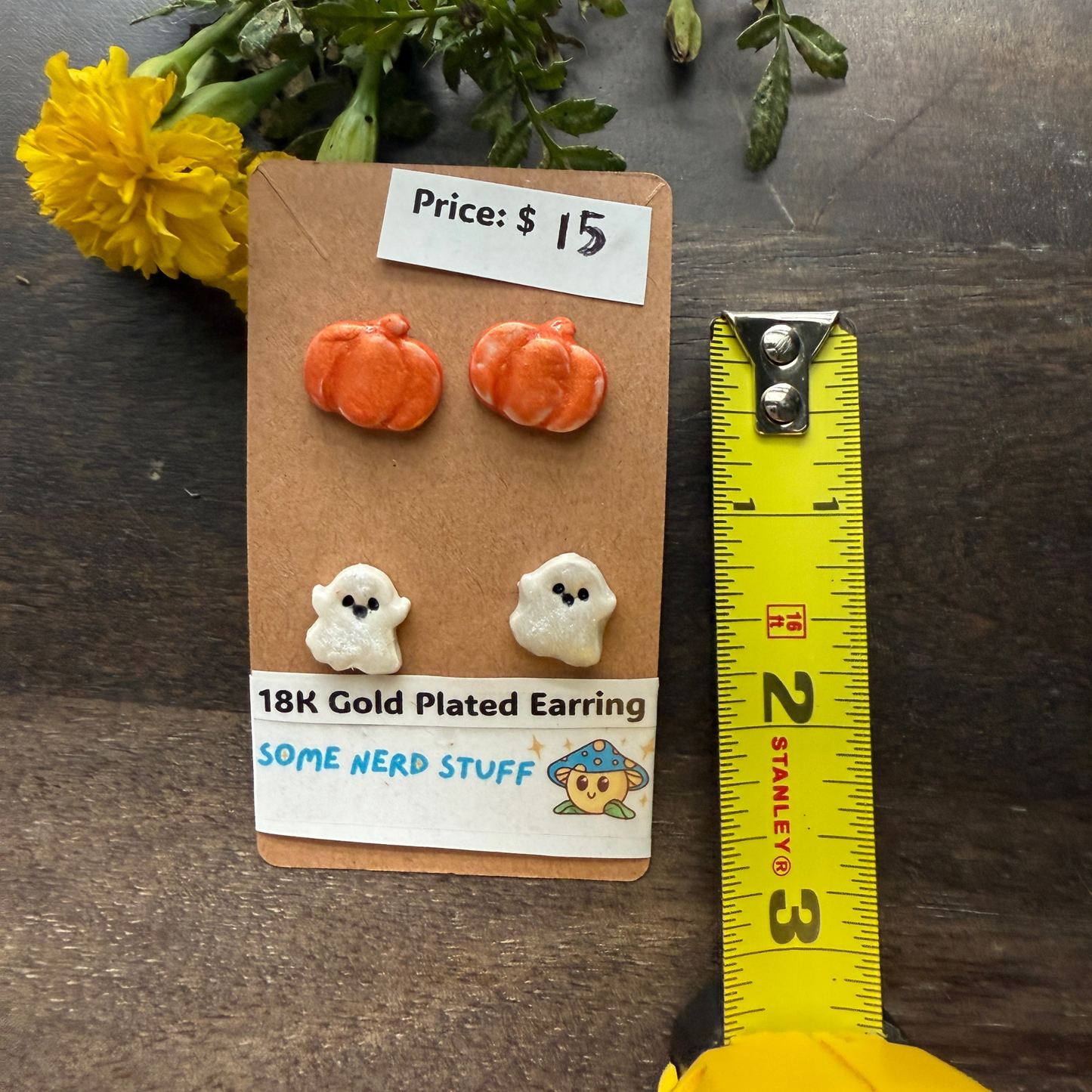 Halloween-themed earrings on a cardboard backing with a price tag, on a wooden surface featuring pumpkins and happy ghosts 18k gold plated earrings.
