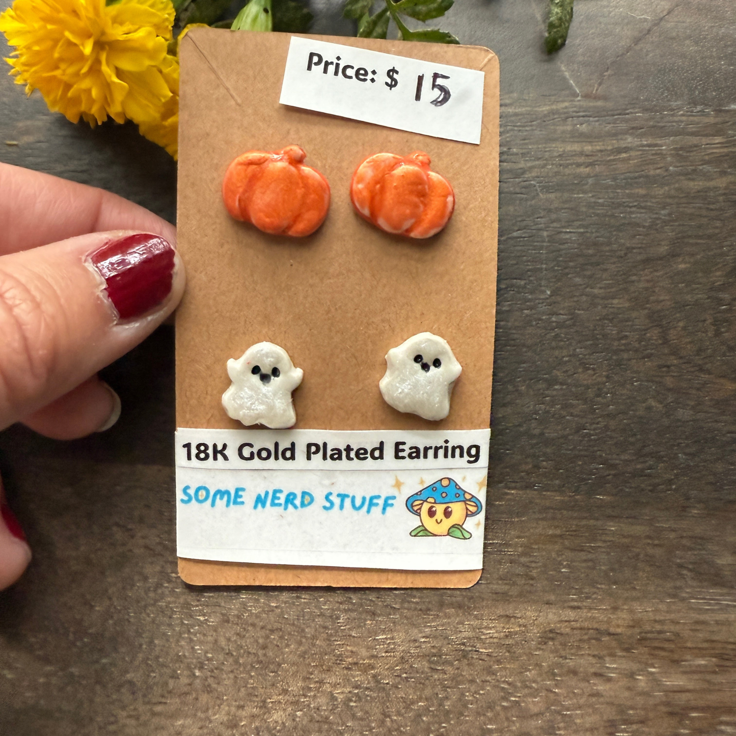Halloween-themed earrings on a cardboard backing with a price tag, on a wooden surface featuring pumpkins and happy ghosts 18k gold plated earrings.