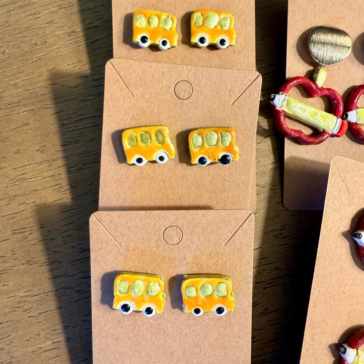 Several pairs of yellow school bus stud earrings with black wheels displayed on kraft cards.