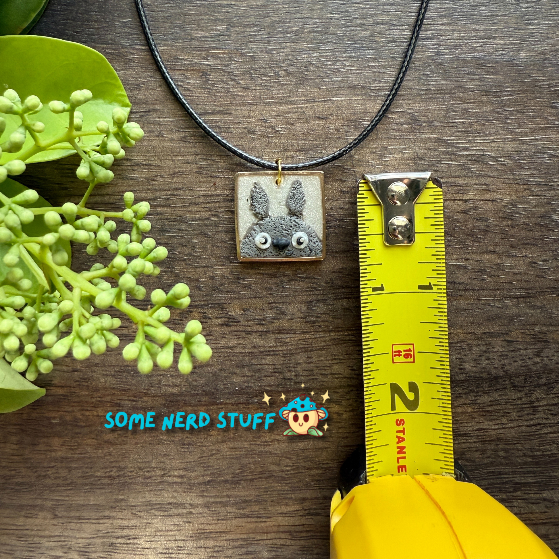 Polymer Clay Charm totoro in a metal square frame handing from a necklace with clasps shown with measuring tape made by SomeNerdStuff