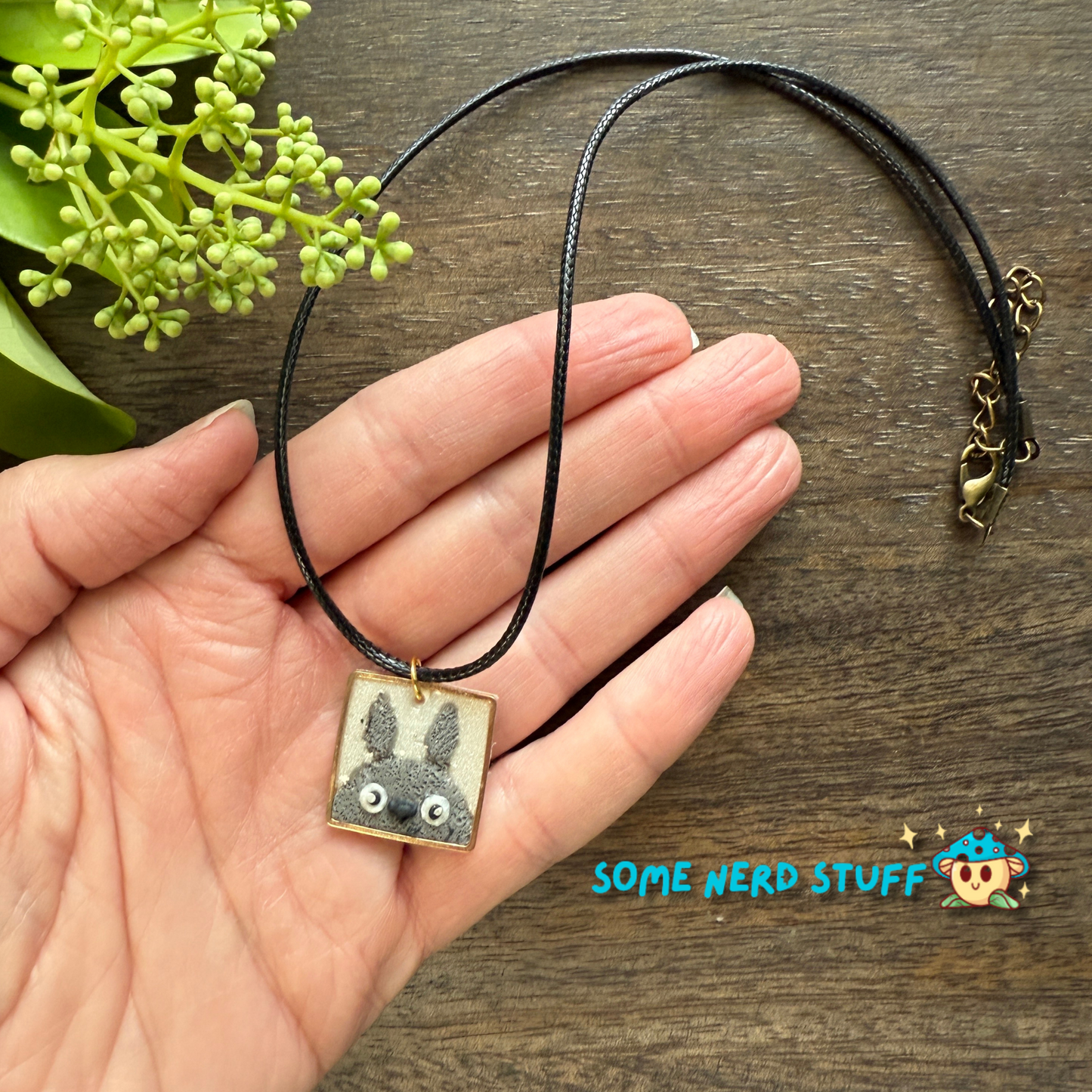 Polymer Clay Charm totoro in a metal square frame handing from a necklace with clasps shown with hand for size made by SomeNerdStuff