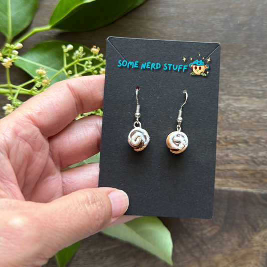 Cinnamon roll earrings made from polymer clay and resin shown in hand for size by SomeNerdStuff