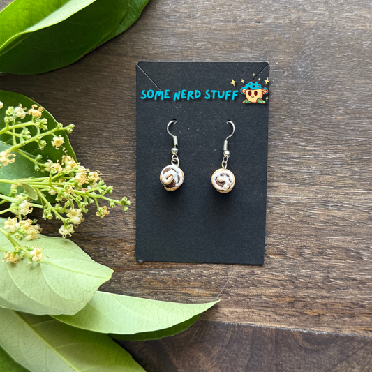 Cinnamon roll earrings made from polymer clay and resin shown in hand for size by SomeNerdStuff