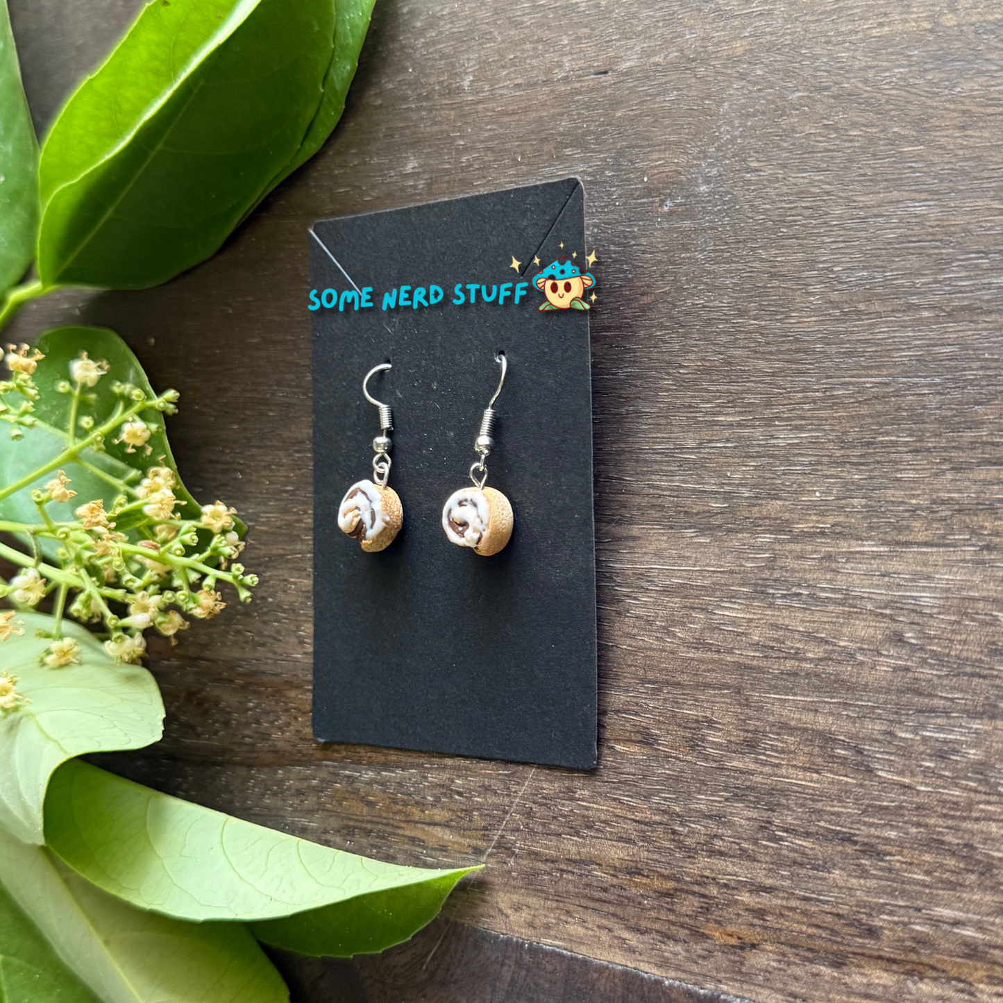 Cinnamon roll earrings made from polymer clay and resin shown in hand for size by SomeNerdStuff