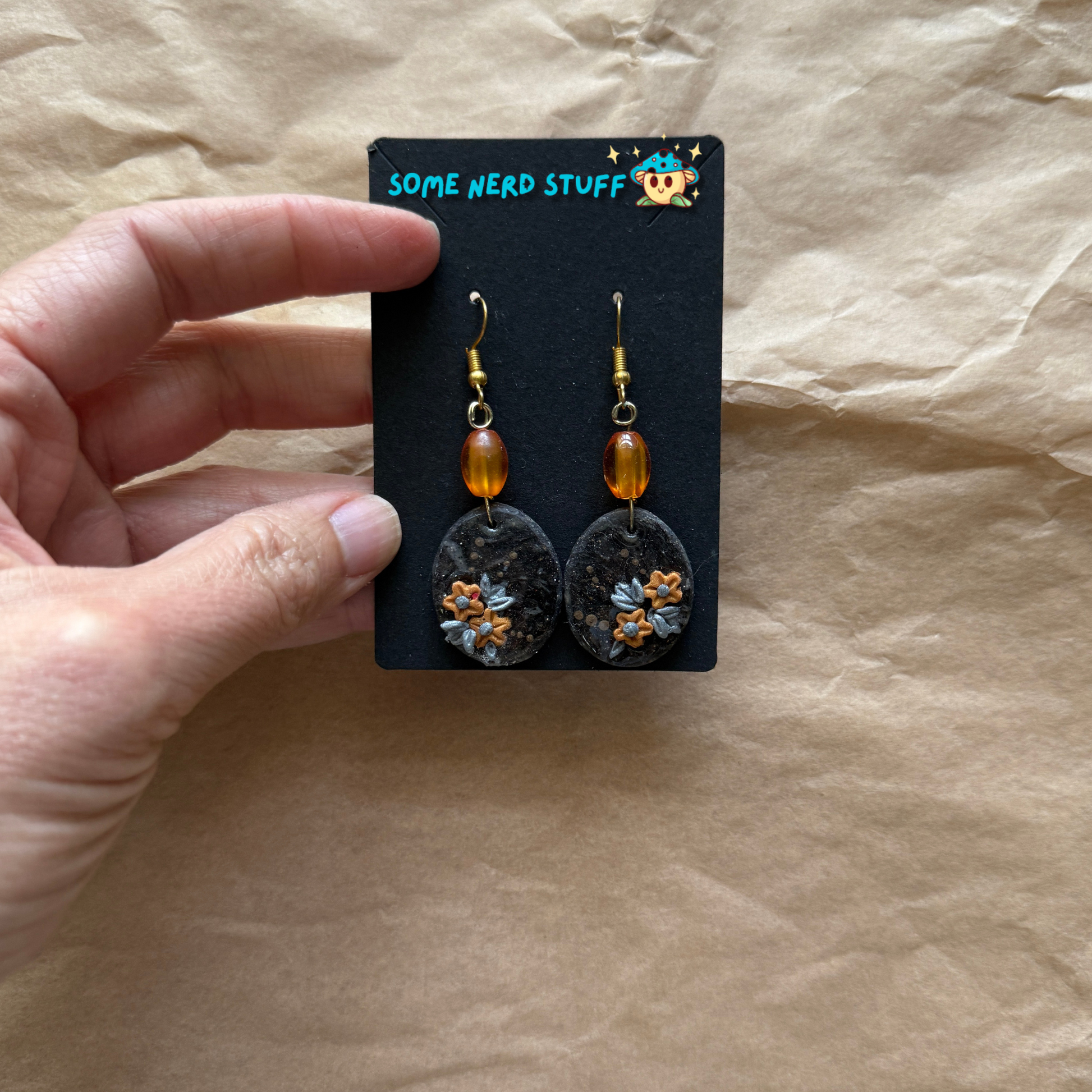 Faux Stone Polymer Clay Earrings with accent flowers and amber beads shown with hand holding them to show size made by SomeNerdStuff