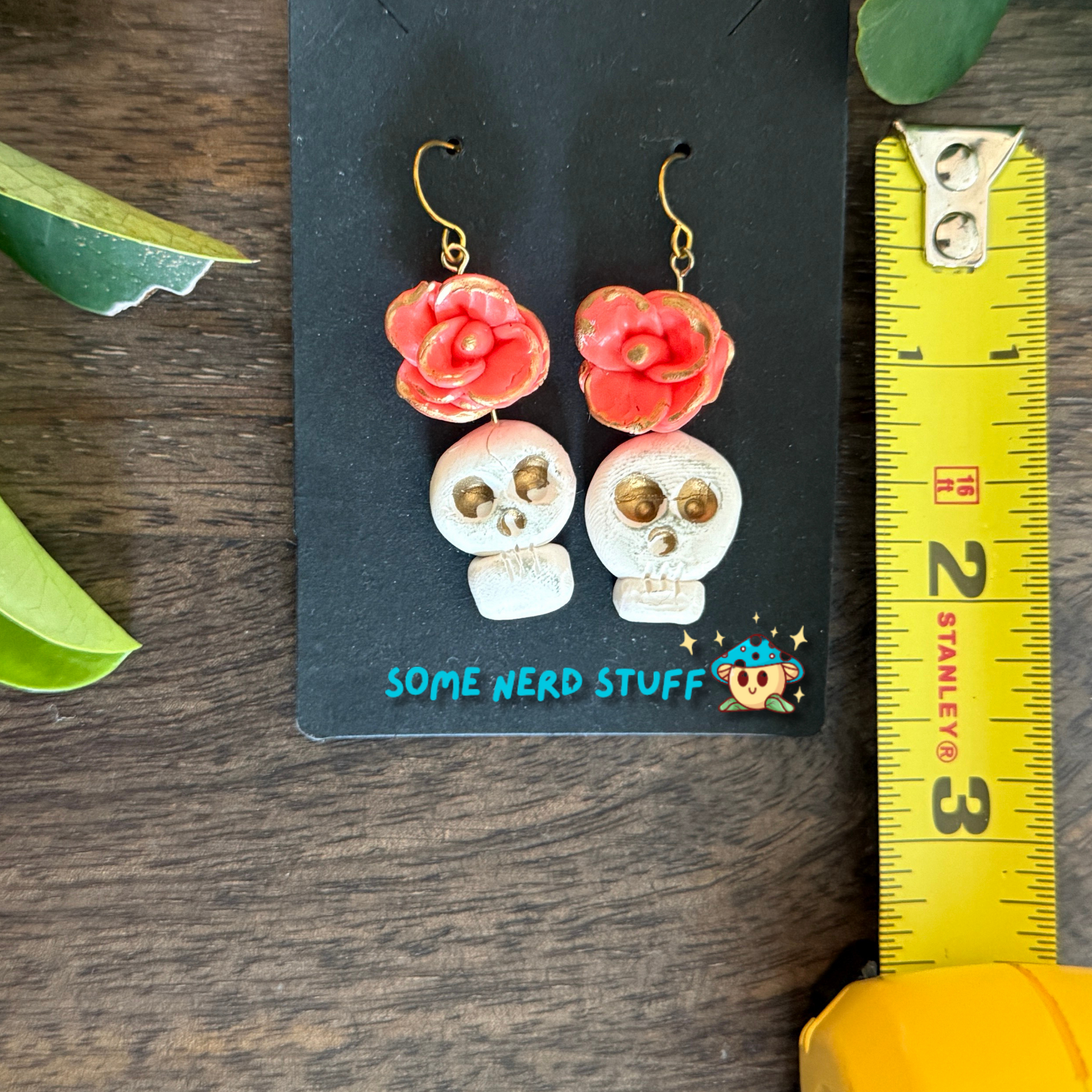 Polymer Clay Wild Rose and Aged Skull highlighted with gold Earrings shown with measuring tape made by SomeNerdStuff