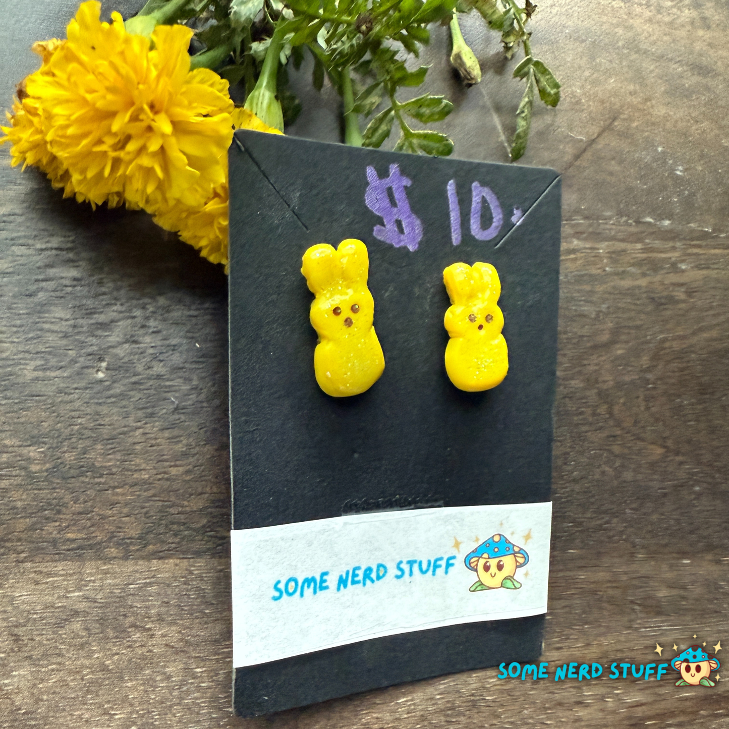 Yellow bunny-shaped polymer clay earrings on a 'Some Nerd Stuff' branded card with a yellow flower in the background.