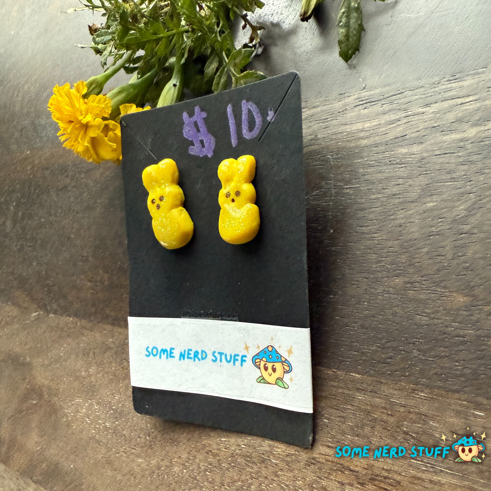 Yellow bear-shaped polymer clay earrings on a 'Some Nerd Stuff' branded card with flowers in the background.