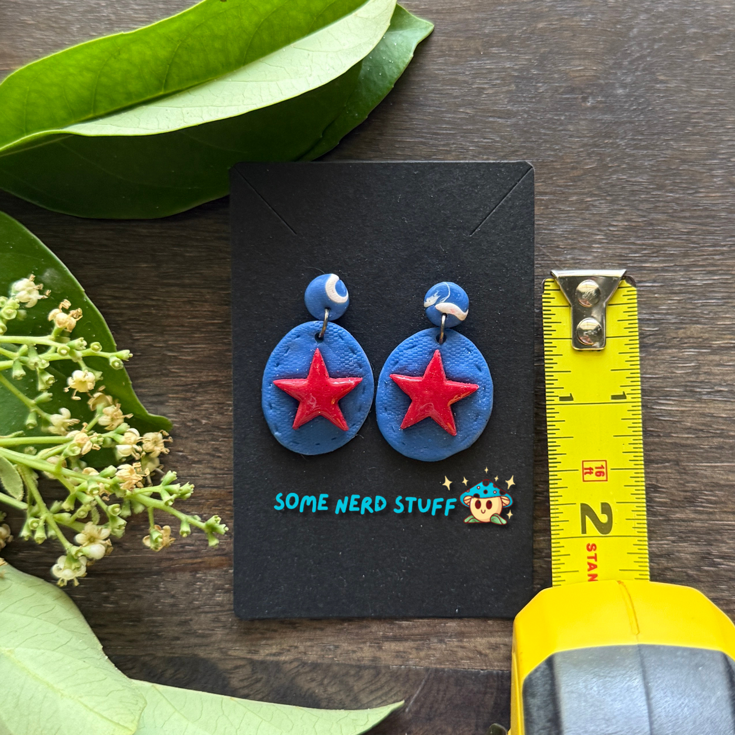 Super hero polymer clay inspired blue and red star earrings shown with measuring tape made by SomeNerdStuff