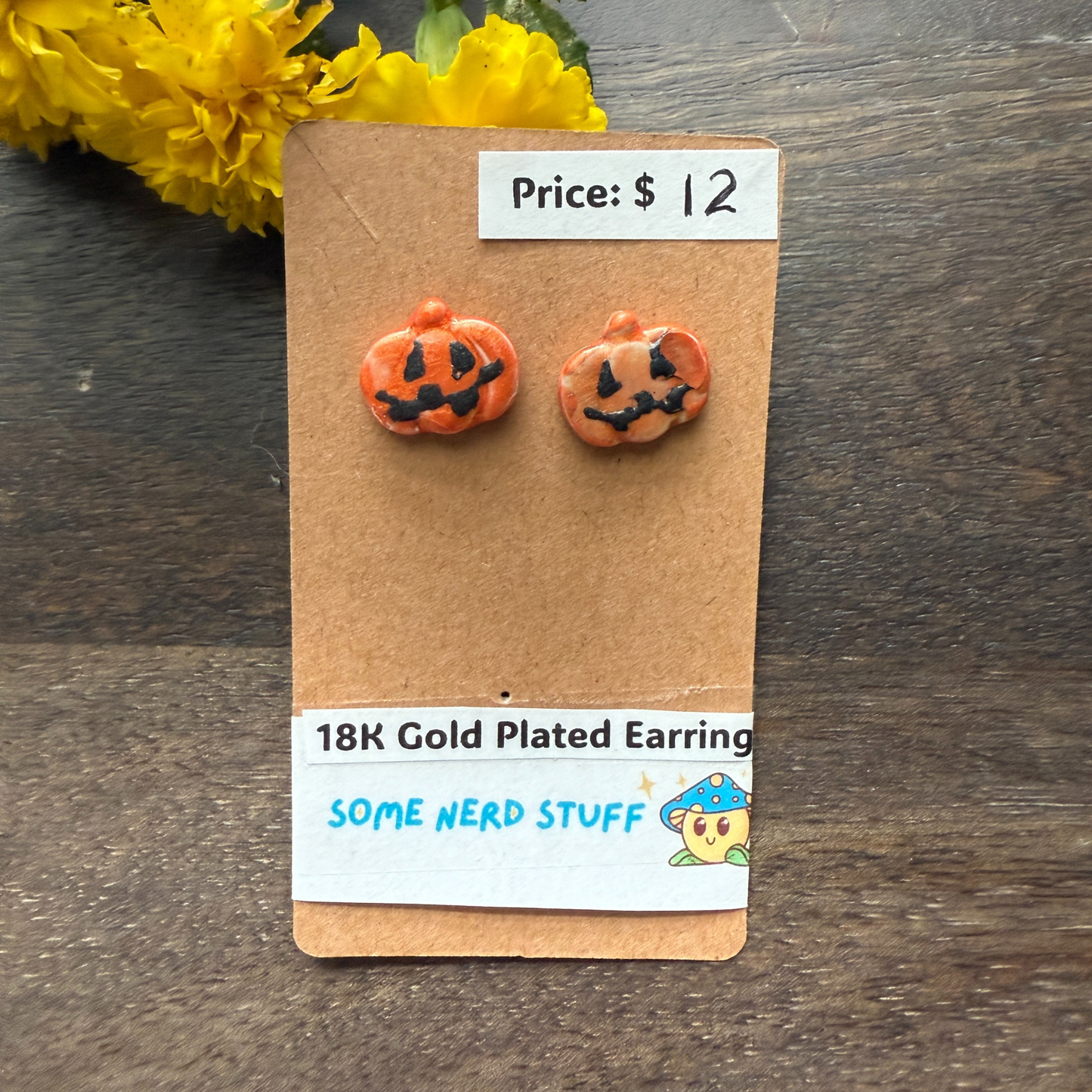 Halloween-themed pumpkin earrings on a cardboard backing with price and 18k plated earrings