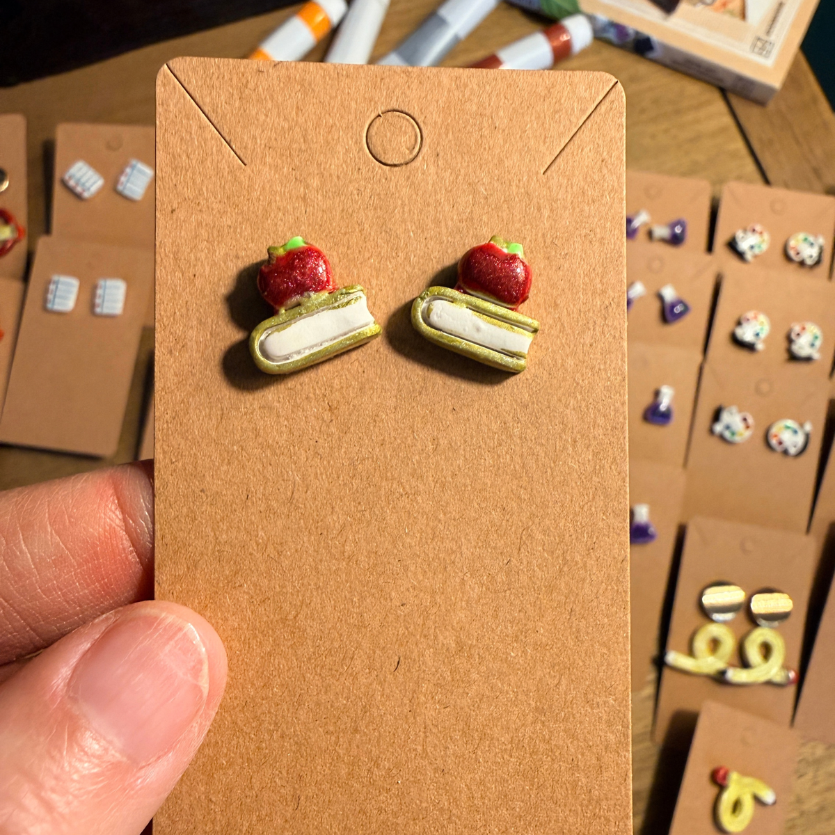 Hand holding a card with matching apple and book stud earrings.